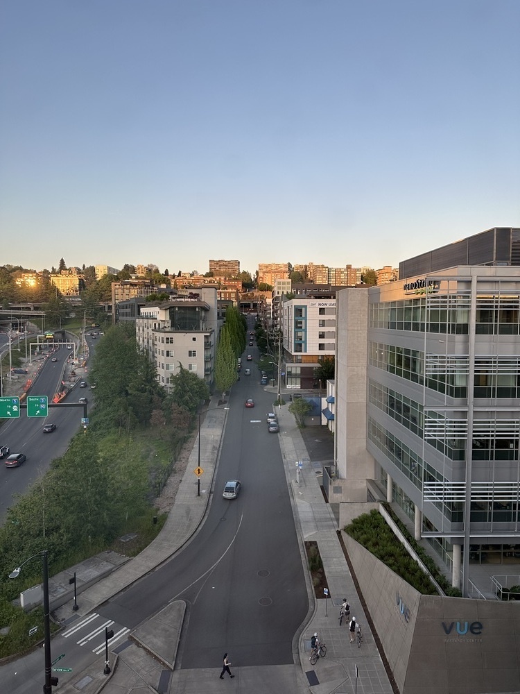 A street leads straight away, up a steep hill lined by six and seven story buildings. The sun is low, just hitting the tops of the buildings. 