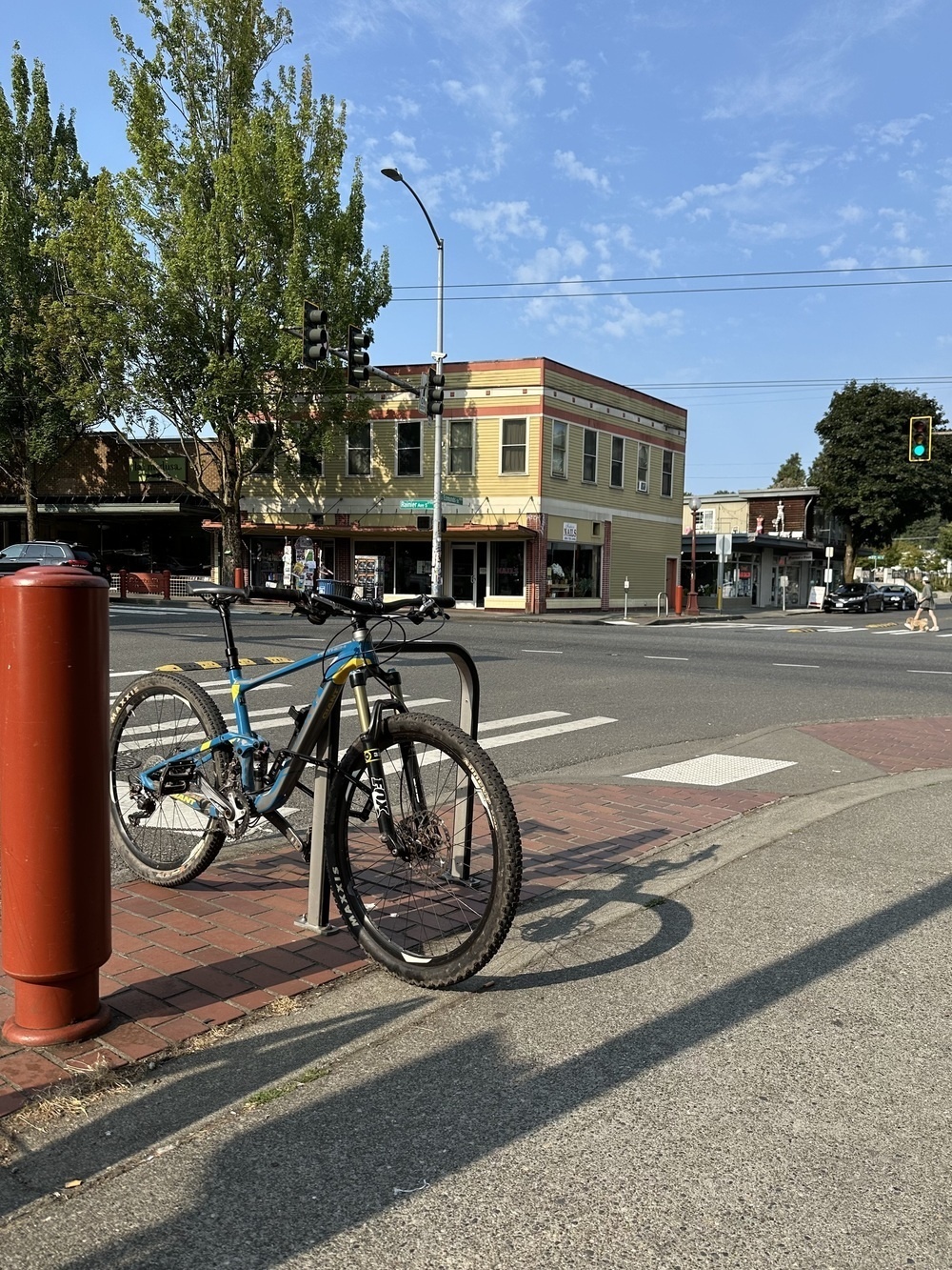 A silvery and blue mountain bike locked to a rack on a sunny street corner.