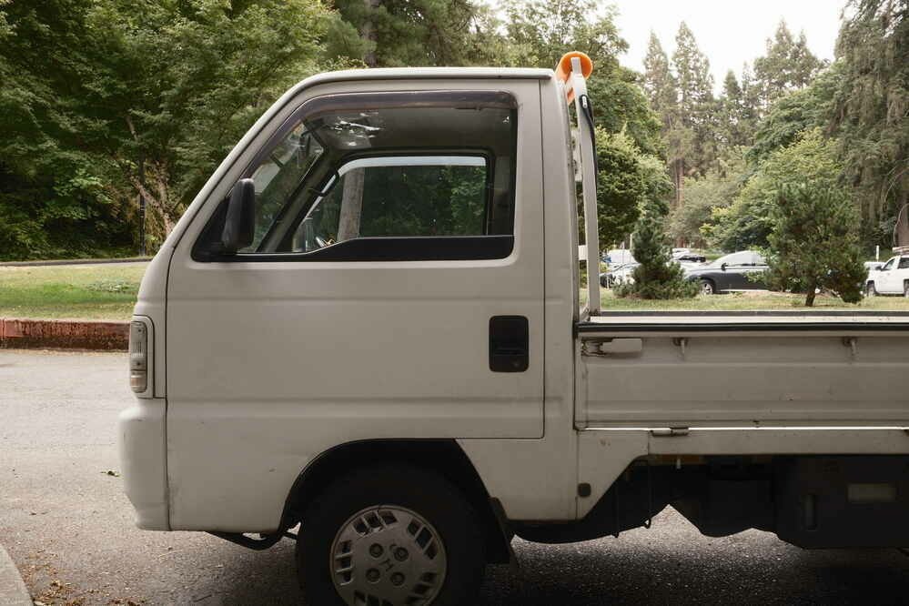 The front end of a white Kei, a cute work truck with a tiny cab and short bed.