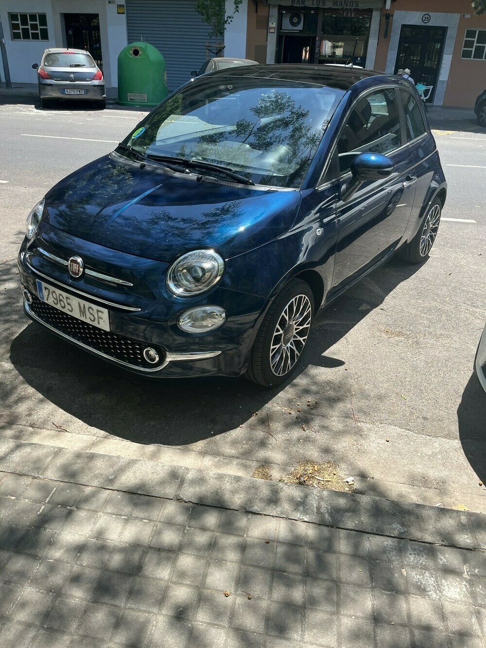 A metallic blue Fiat 500 parked in a sunny city street in Spain. 