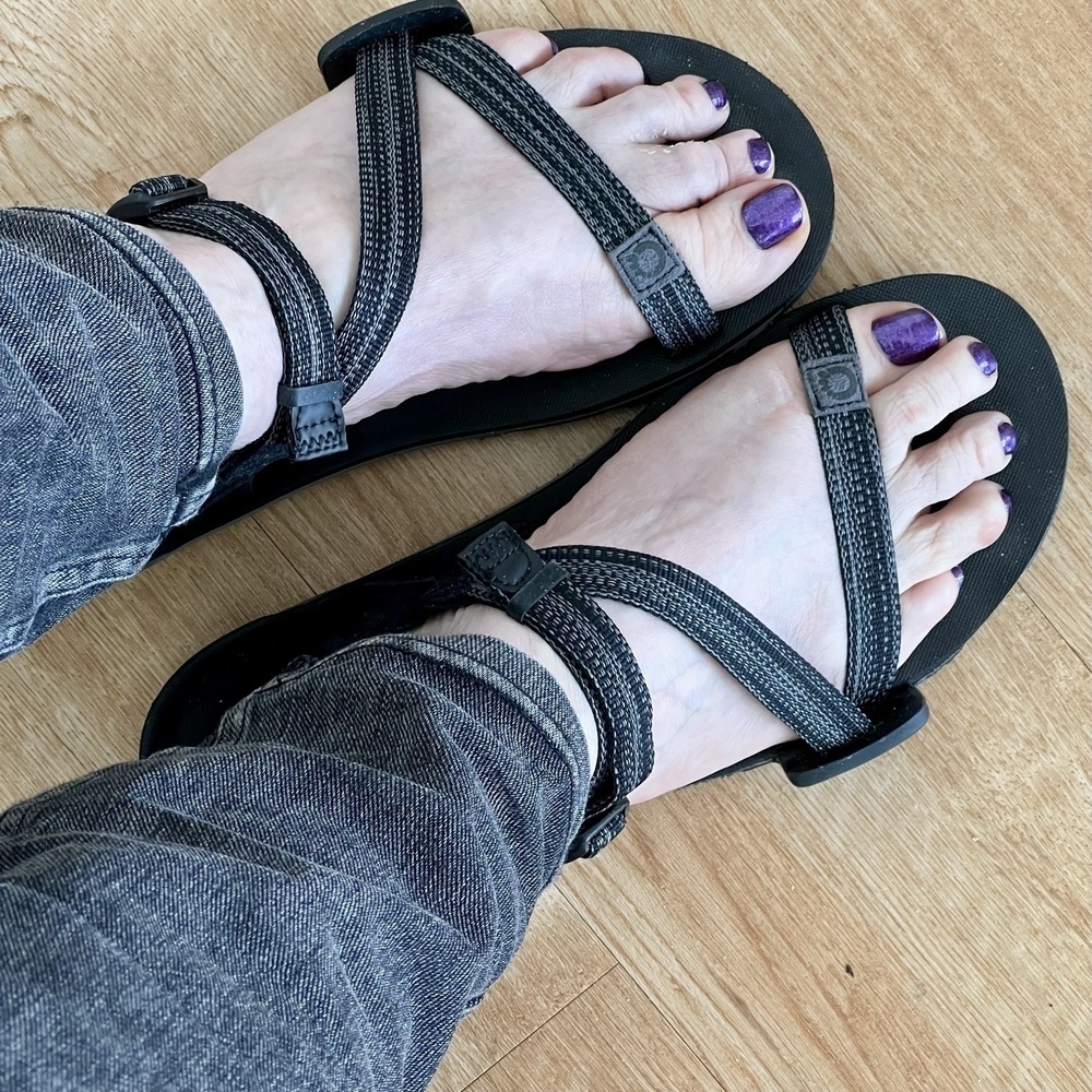 Two feet in sandals with iridescent dark purple polished toenails