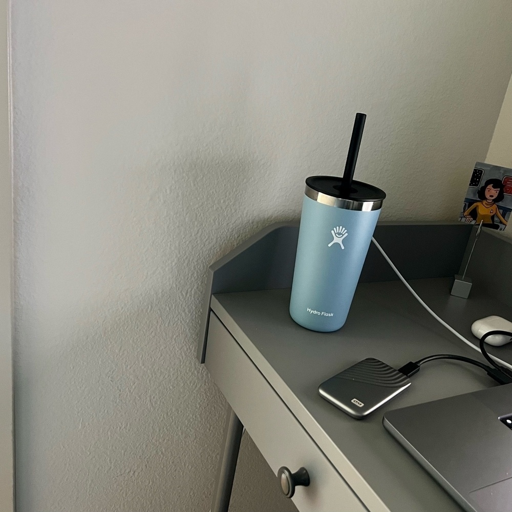 20 oz light blie Hydro flask with black straw on desk near my Mac. 