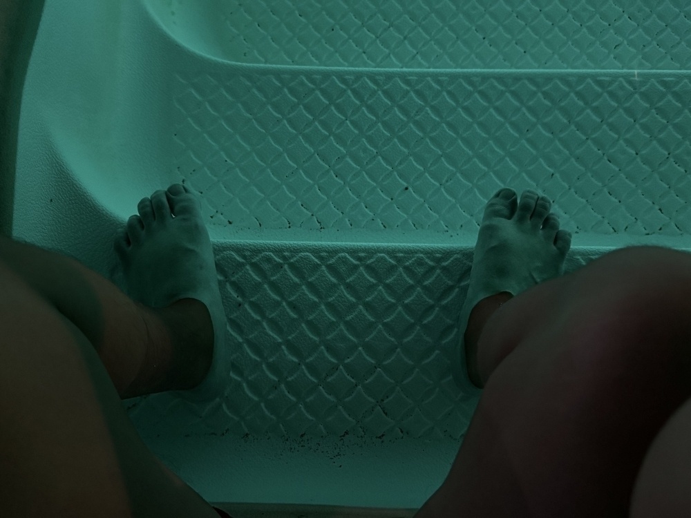 The image shows a close-up of two feet on textured steps, illuminated by greenish light, likely indicating an underwater environment such as a pool.