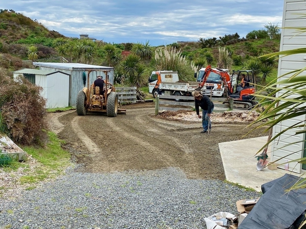 Tractor with grading blade, digger and trucks work on the driveway.