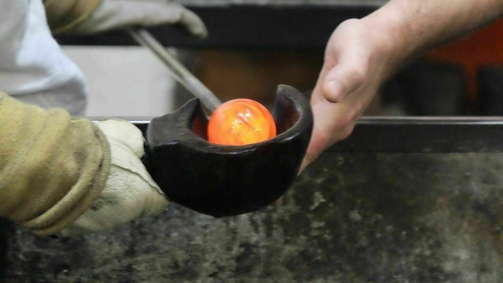 Hands, gloved and ungloved, cupping a red hot glass globe. 