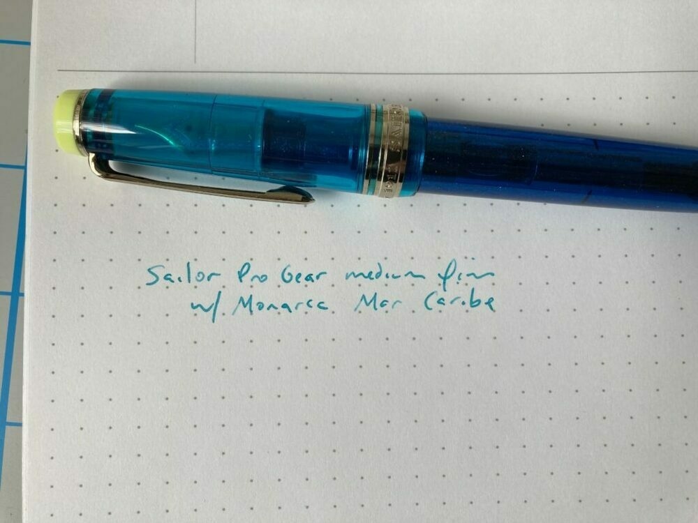 Sailor Pro Gear pen sitting on top of an open Maruman Mnemosyne notebook. on the page is written "Sailor Pro Gear medium fine w/Monarca Mar Caribe"