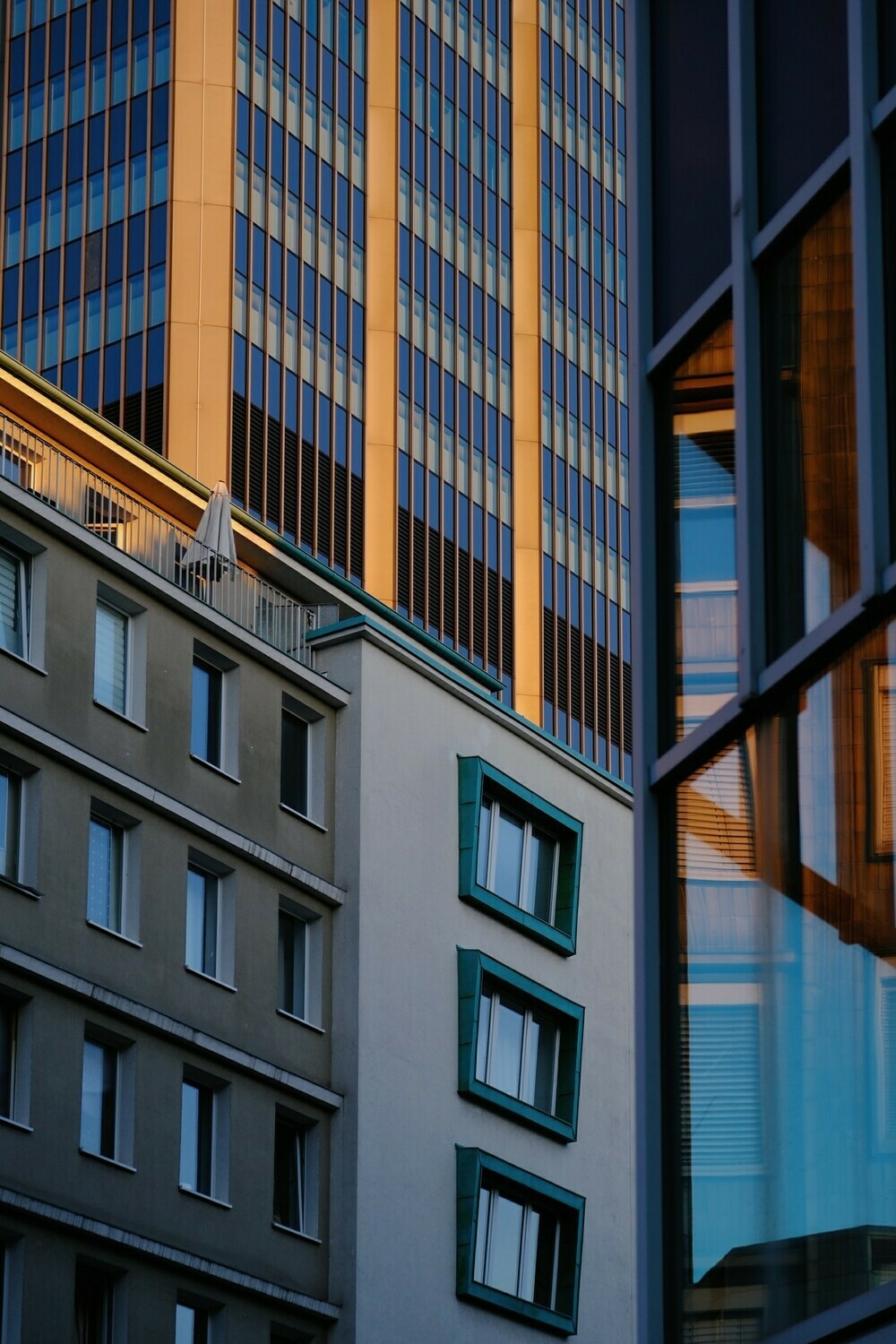 Close up of a series of buildings, their frontages overlapping and their strong vertical lines intersecting with each other. One of the buildings, fronted with glass, is reflecting a fourth building.