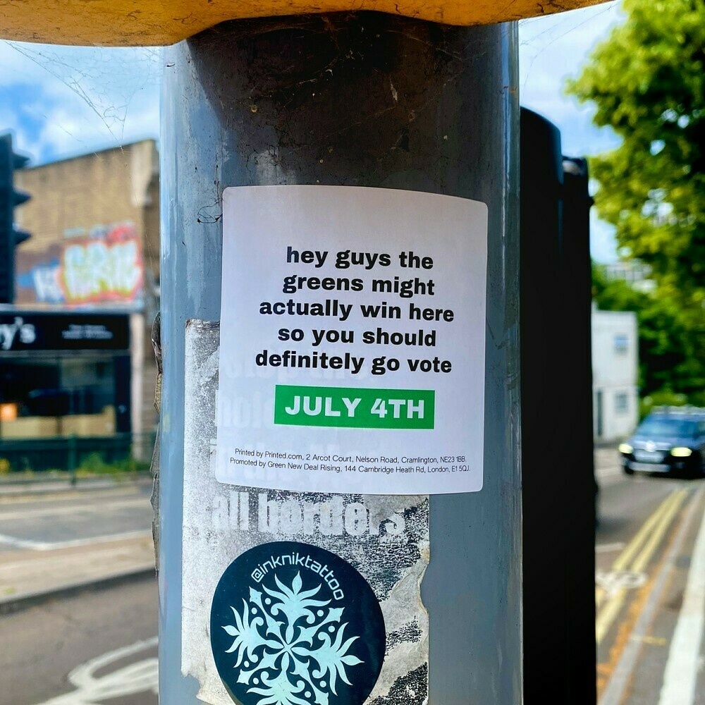 A sticker on a traffic light pole that reads ‘hey guys the greens might actually win here so you should definitely go vote. July 4th’.