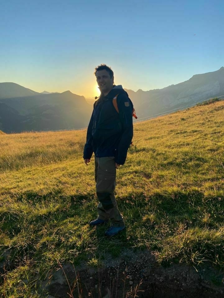 Me wearing trekking gear in the mountains. In the backround, the sun is rising.