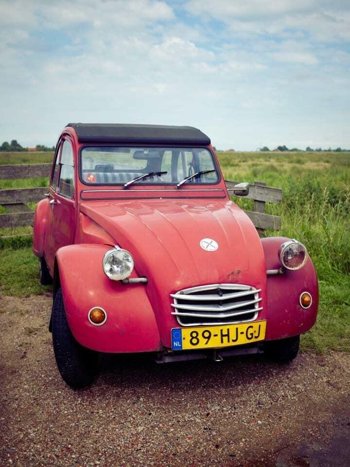 A red Citreon 2CV parked by a green field.