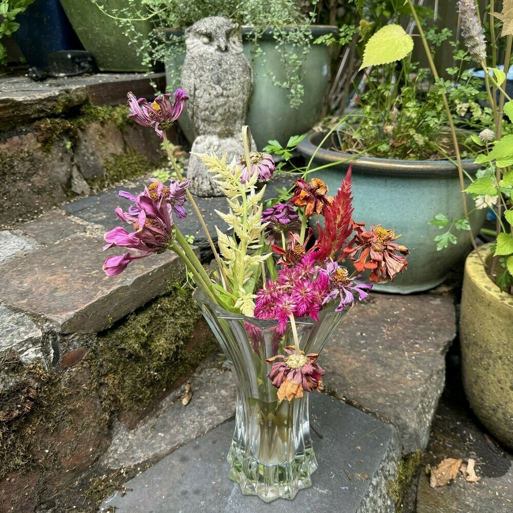 Vase full of wilted flowers sitting on porch steps with a concrete owl statue.