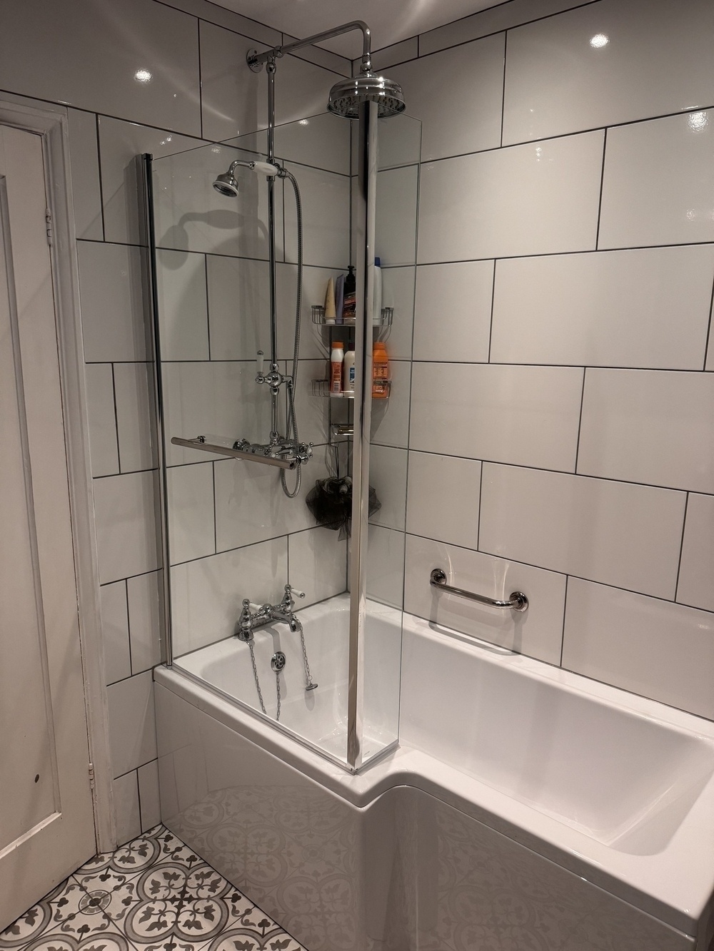 A modern bathroom features a white tiled corner with a bathtub, an overhead shower, and a glass partition.