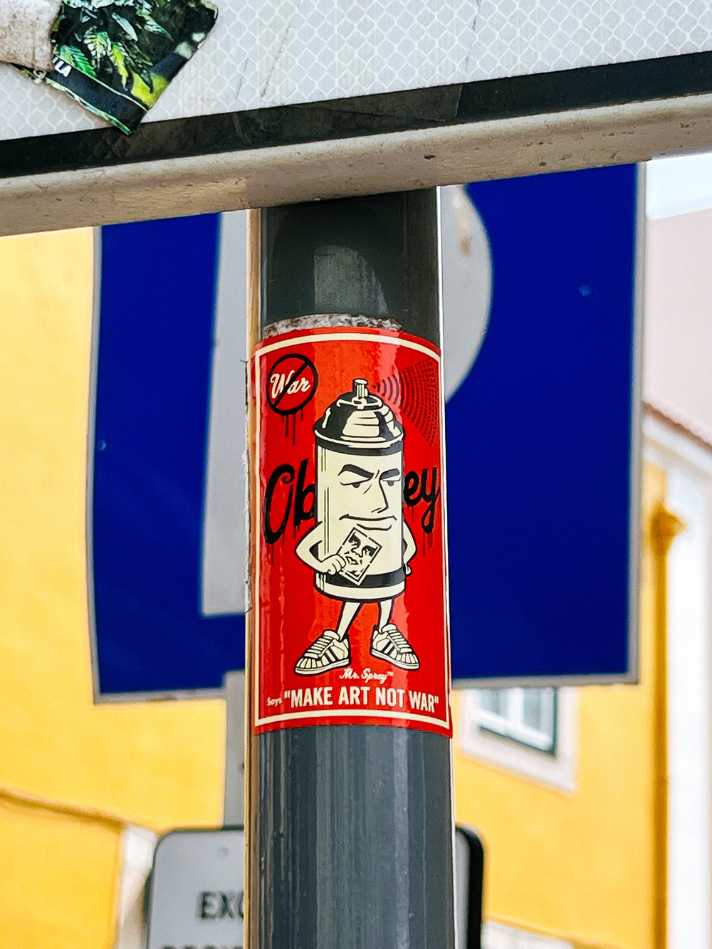 A spray paint can (Mr Spray) holding a copy of Shepard Fairey&rsquo;s OBEY, with &ldquo;make art not war&rdquo; under it. 