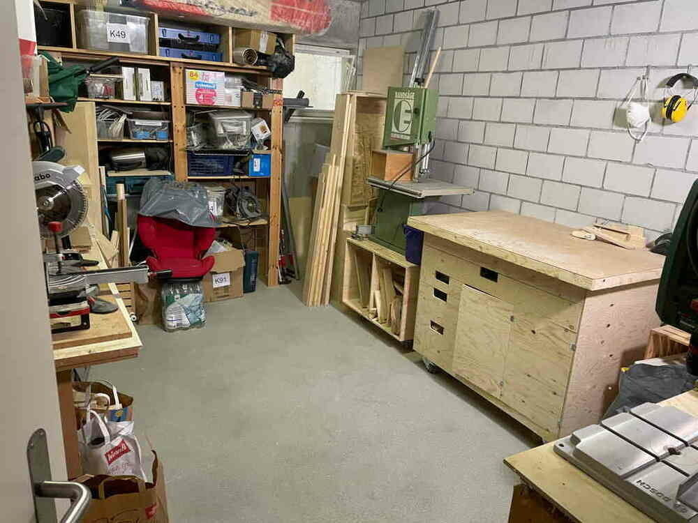 On the right side is my homemade workbench, next to it is the bandsaw. At the far end is a shelf with a lot of stuff. The image is taken from the door. The floor in the middle of the room is empty and clean.