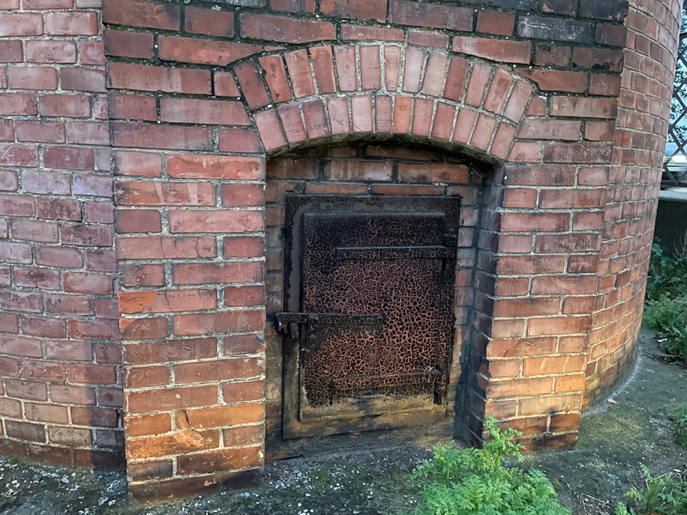 A close-up of a metal door in a read brick wall. The door is nearly black from rust.