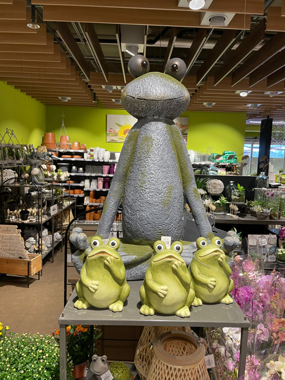 A closeup of a frog statue used as advertising and De oration in a flower store. In front of it are smaller frog sculptures made from sheet metal to buy.