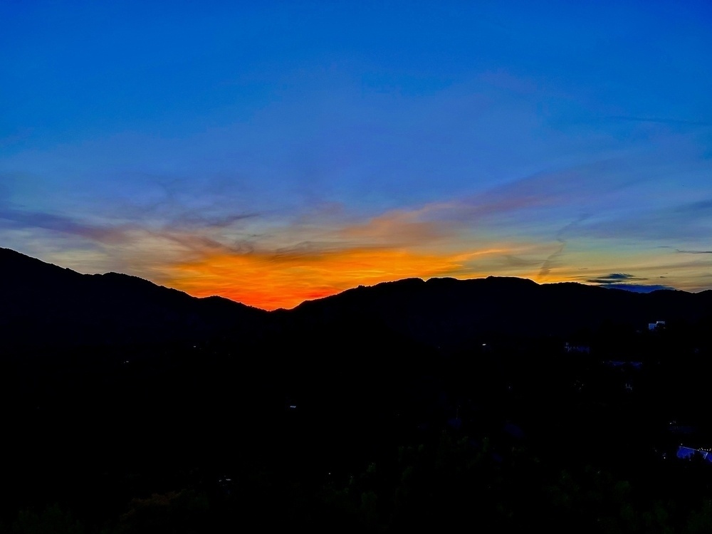 A vivid splash of red and orange sunset over a bright blue sky, jet black mountains in the foreground. 