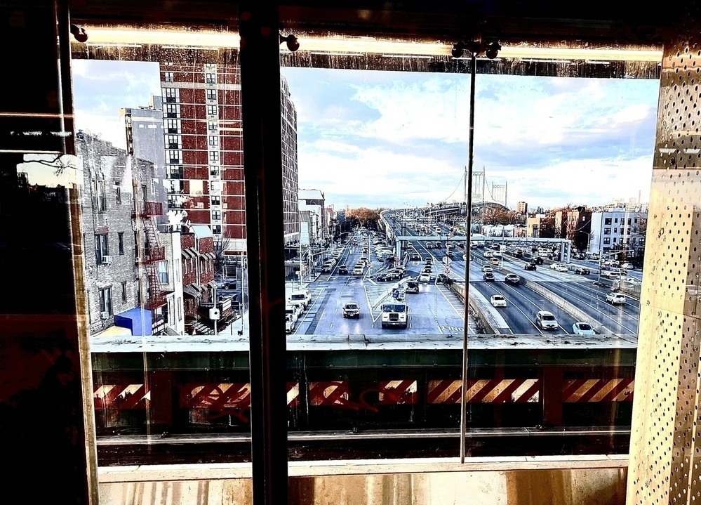 The tri-boro bridge during the day, shot through a glass elevator shaft. 