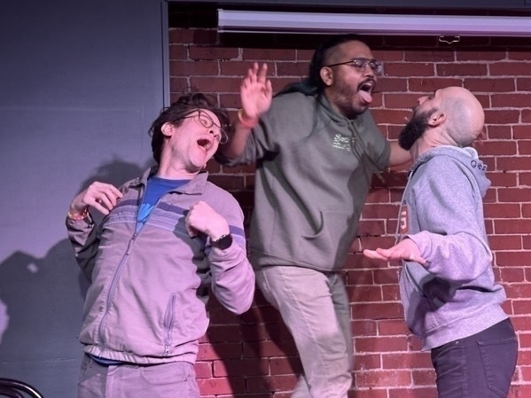 Three men, two white one brown, flapping their arms and opening their mouths like birds against a brick wall.