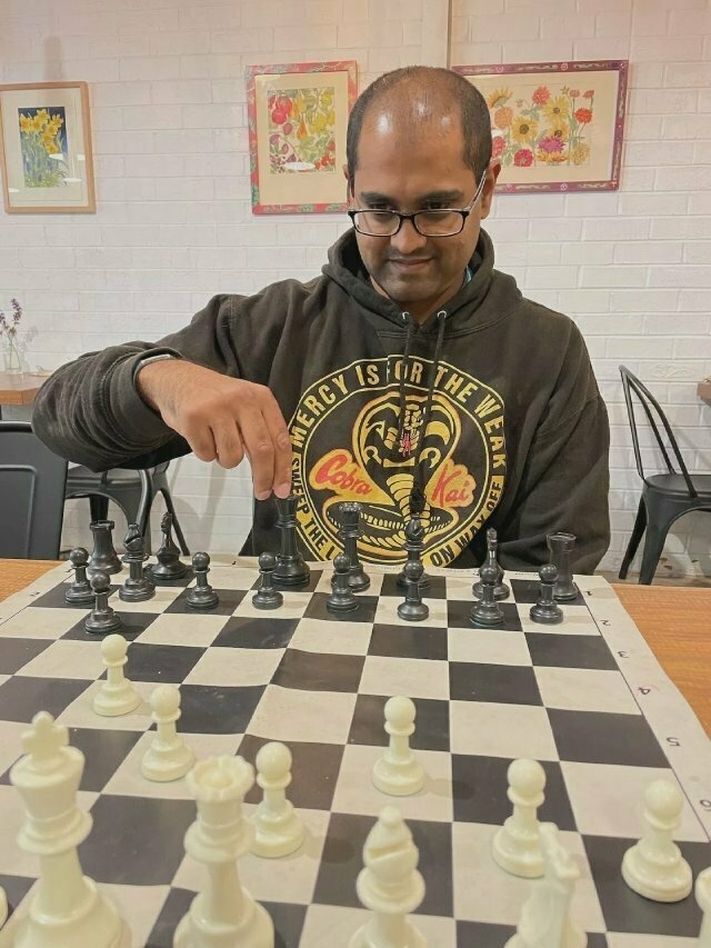 An Indian guy in hoodie and glasses, pondering his next chess move