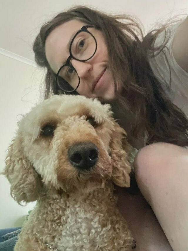 Selfie of a white girl with glasses and long brown hair with a tan-coloured poodle-cross who's looking straight at the camera