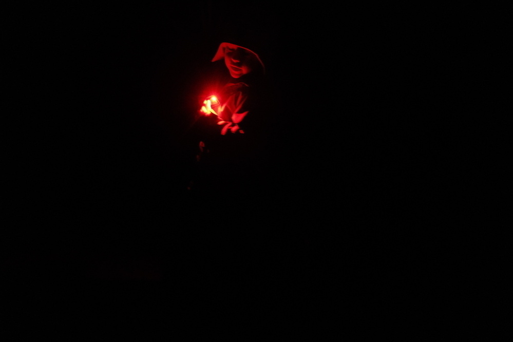 A person wearing a hooded garment is holding a bright red light in a dark environment.