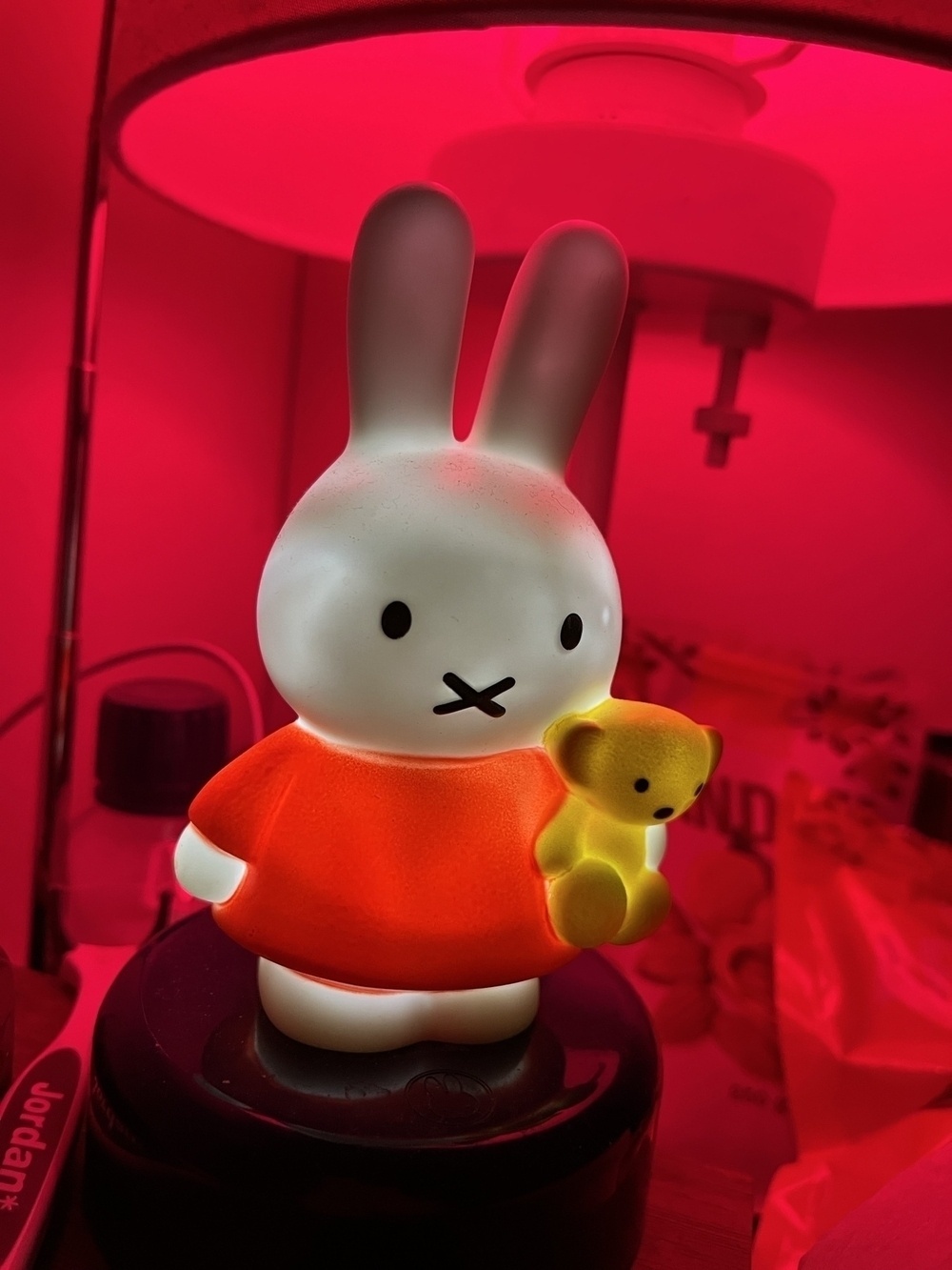 A night stand lamp with red light, Miffy the rabbit night light, and some clutter.