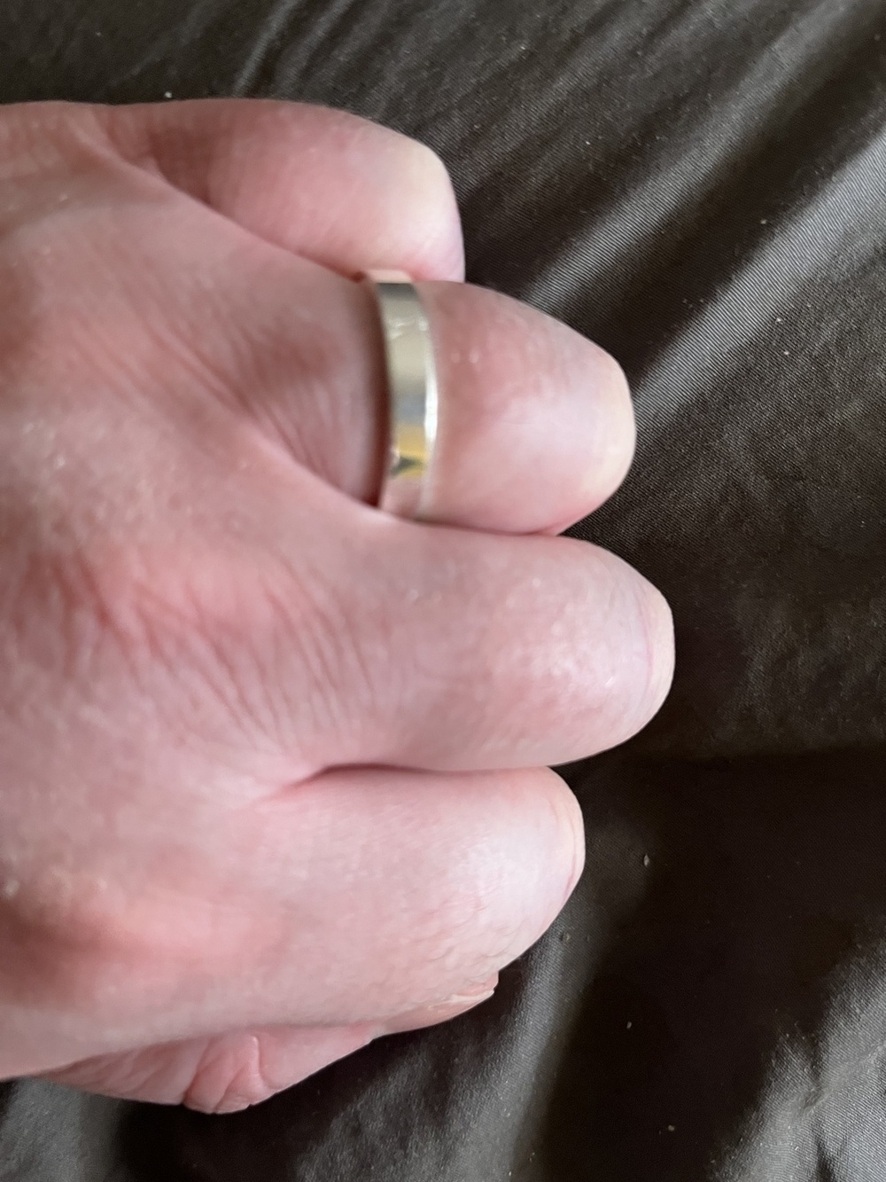 A mans left hand with a silver wedding ring on the ring finger.