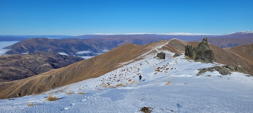 Runner on hill, closer half covered in snow, farther half brown tussock