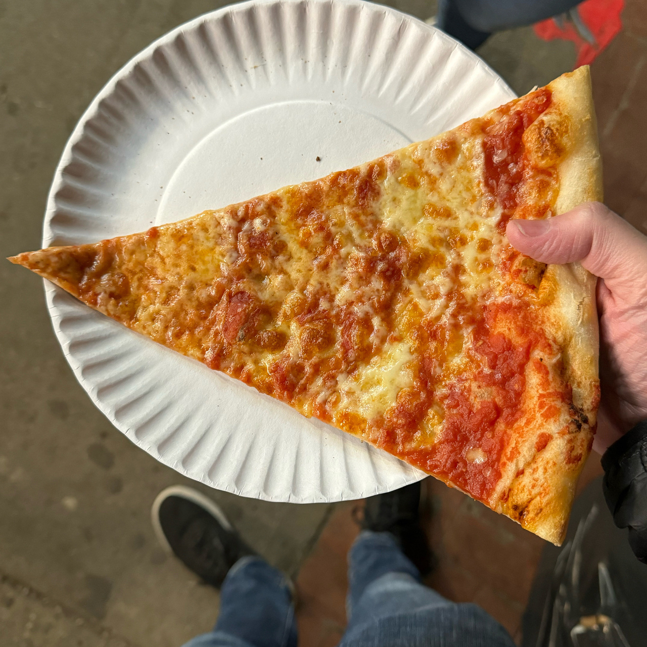 Slice of cheese pizza held in hand on a paper plate
