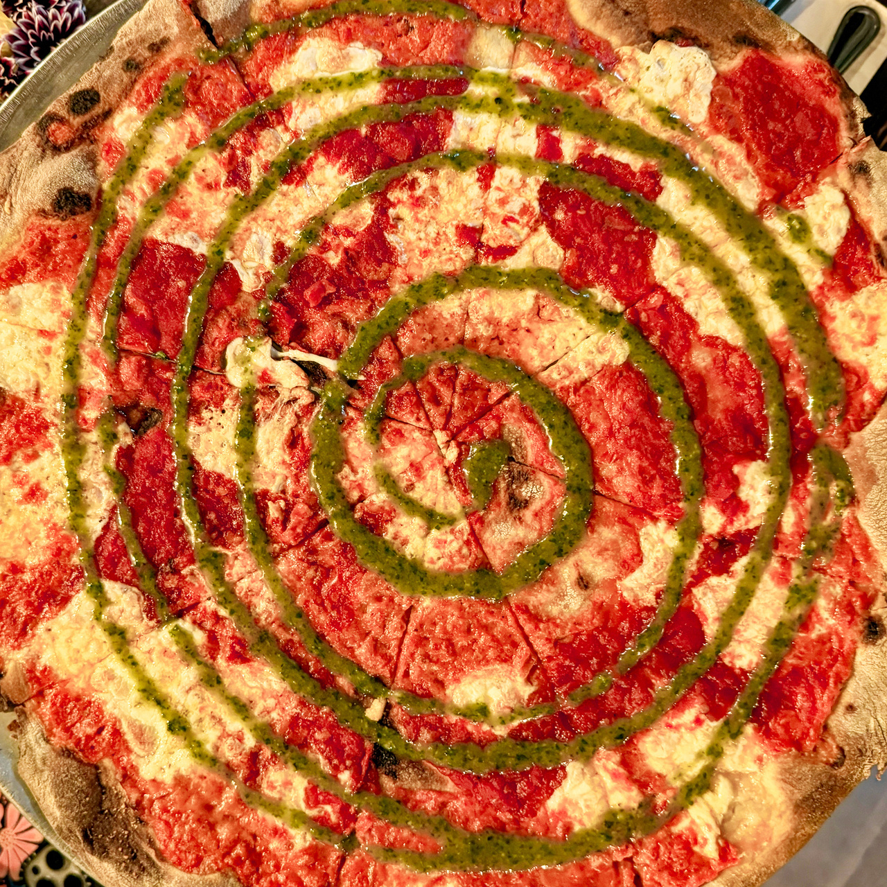 Pizza with vodka sauce, tomato sauce, fresh mozzarella, and a spiral of pesto sauce