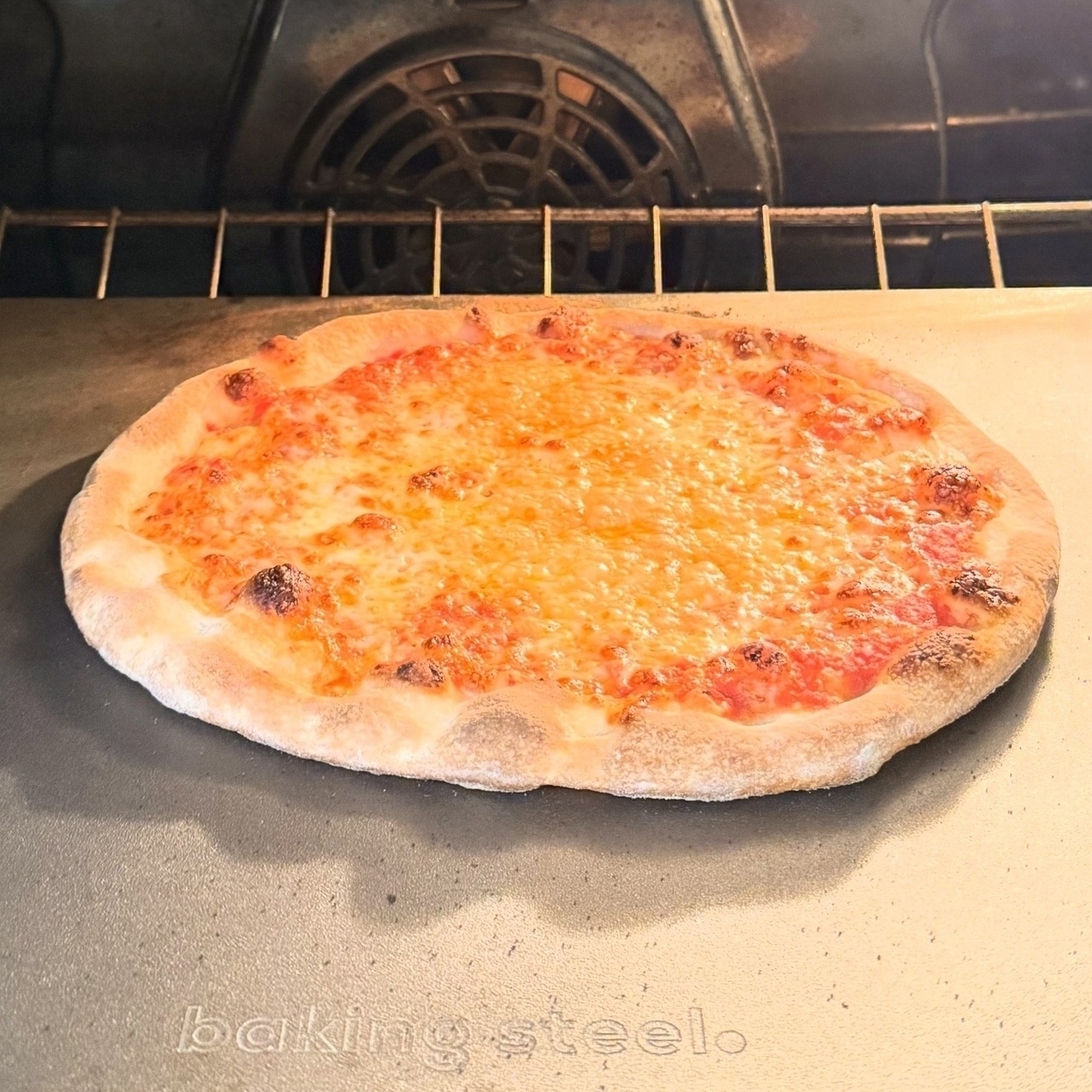 A cheese pizza is baking on a baking steel inside an oven.