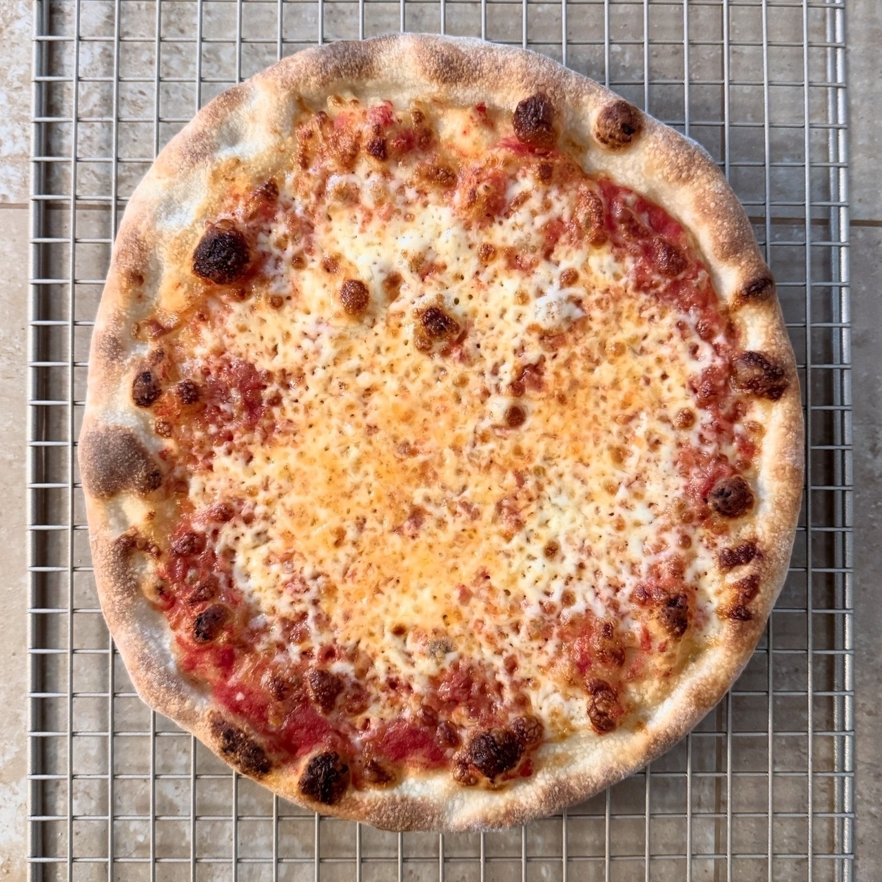 A freshly baked pizza with a golden, bubbly cheese topping rests on a cooling rack.
